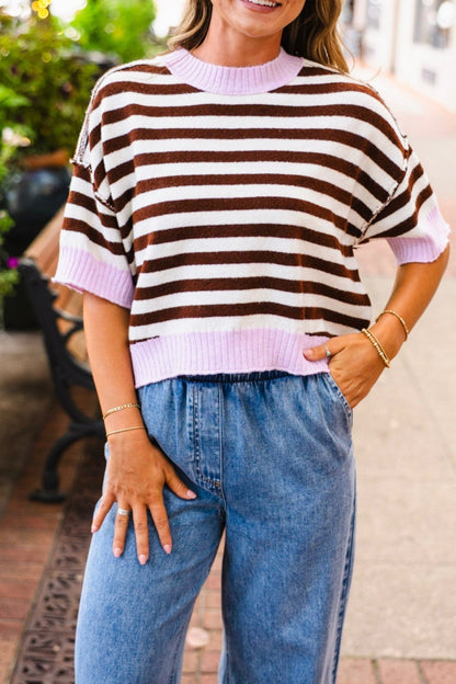 Woman wearing a rib stripe short sleeve sweater in light pink and brown with blue jeans