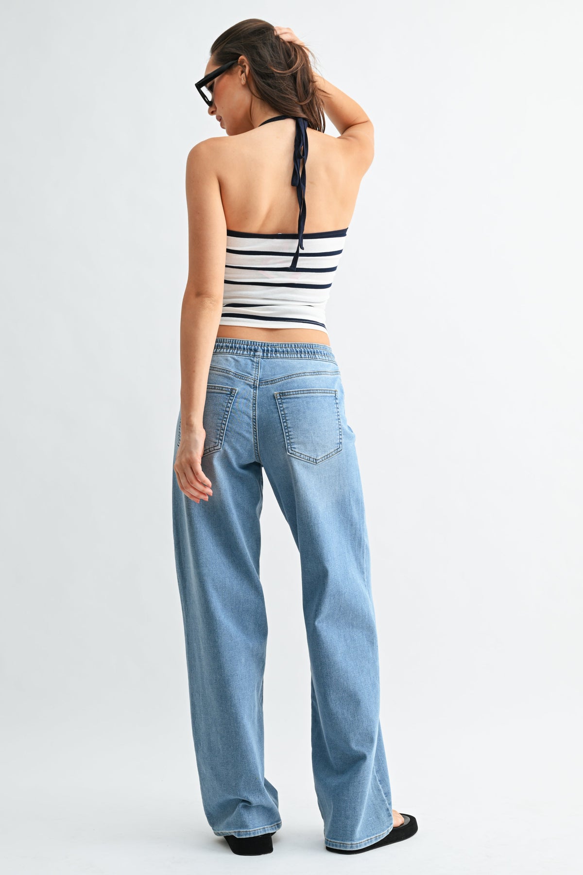 Woman wearing a striped halter top and light blue pull on jeans on a white background