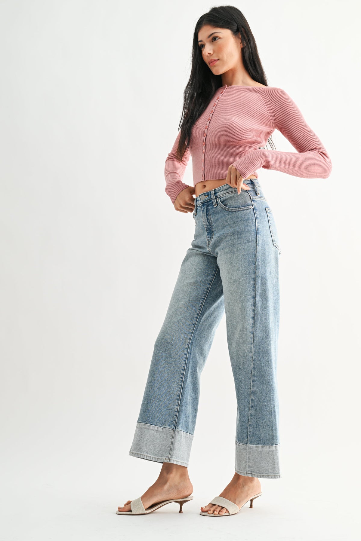 Woman wearing a pink long-sleeve top and light denim two toned wide-leg blue jeans with bone colored heels on a white background 