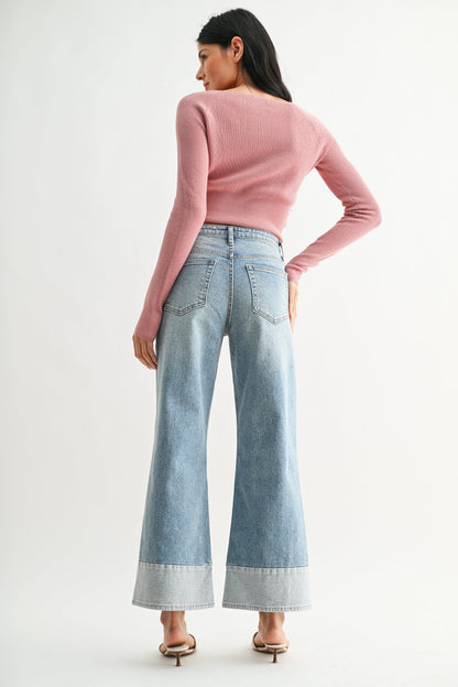 Woman wearing a pink sweater and light denim wide leg two toned hem seamed blue jeans on a white background