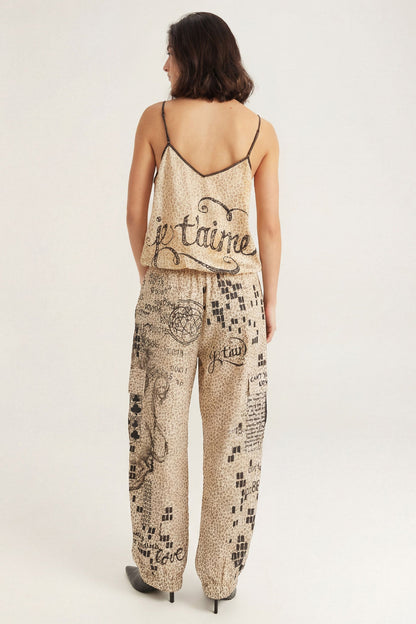 A woman shown from the back wearing a beige and black patterned camisole top with 'je taime' written across the back and matching cargo pants with a black graphic Noir Muse print, set against a plain light gray studio background.