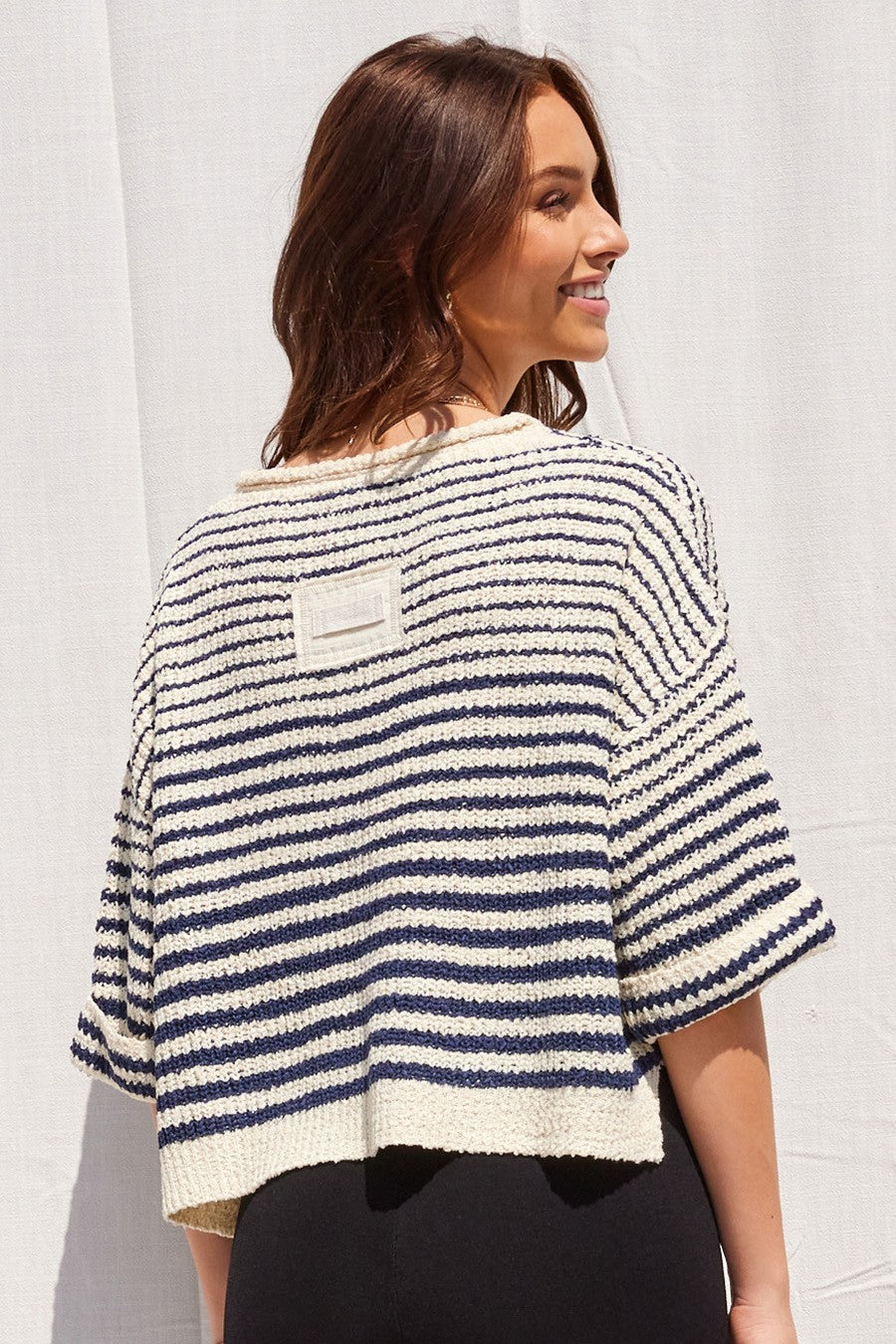 A woman wearing a navy ecru striped knit sweater top, shown from the back against a white textured wall.