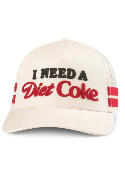 An off-white trucker hat with 'I NEED A Diet Coke' embroidered on the front. The text 'I NEED A' is in black, 'Diet Coke' is in red script, and there are red and black stripes on the side mesh panels.