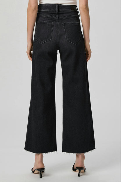 Rear view of a model wearing Anessa ink black wide-leg cropped jeans with a frayed hem and back pocket details, paired with black heeled sandals against a light gray studio background.