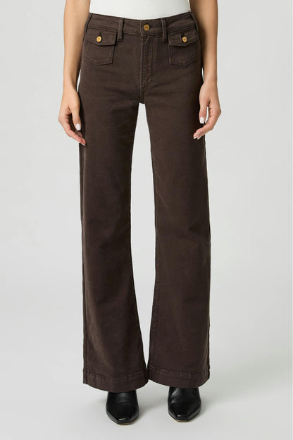 A person wearing Leenah rich chocolate brown wide-leg pants with front flap pockets and gold-tone buttons, shown from the waist down against a light gray studio background.