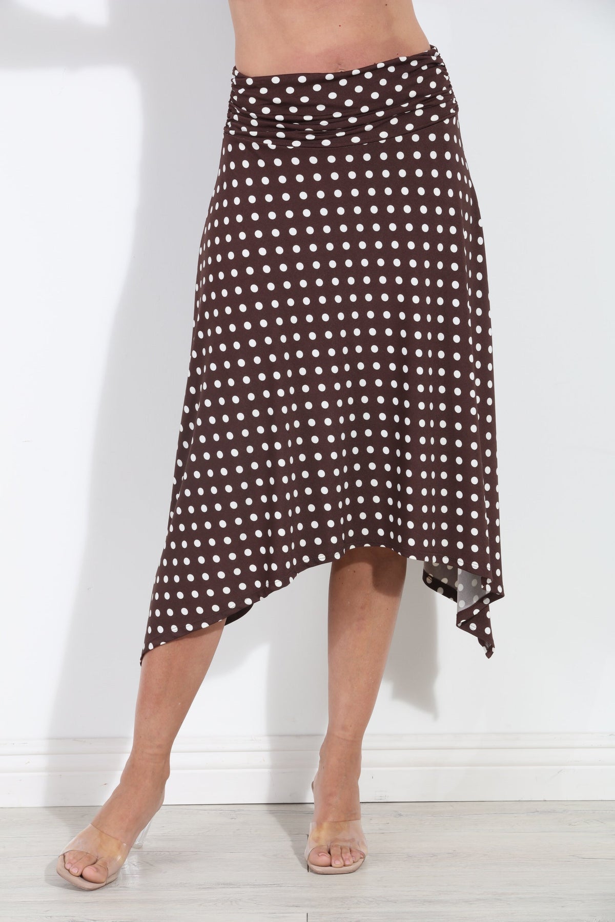 A brown and white polka dot wrap midi skirt worn by a model, shown from the waist down against a white wall.