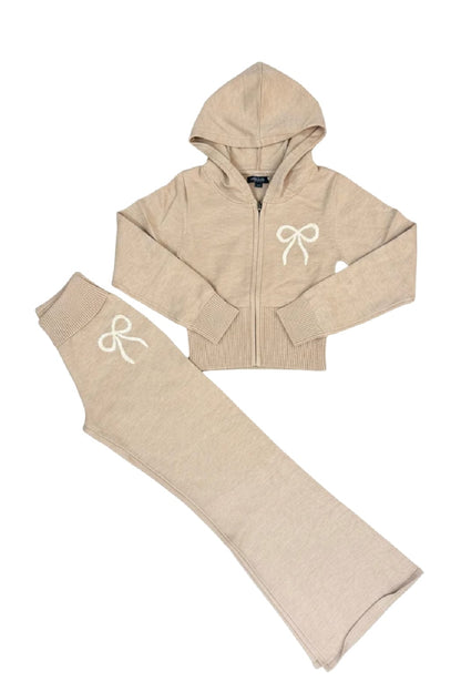 A two-piece children's knit loungewear set in an oatmeal color, featuring a zip-up hooded sweatshirt and matching flared pants, both with a white embroidered bow on the chest and thigh.