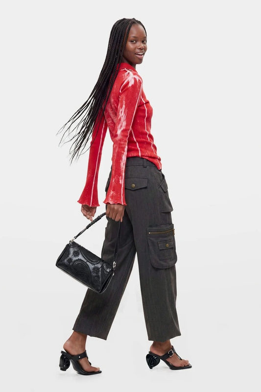A woman modeling a red long-sleeve tie-dye top, dark gray cargo pants, and black heeled sandals, carrying a black quilted textured handbag against a light gray studio background.