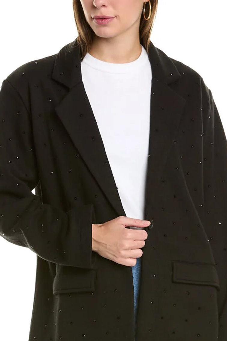 A woman wearing a black open-front blazer with small embellishments, layered over a white crewneck top and blue jeans, against a plain white background.