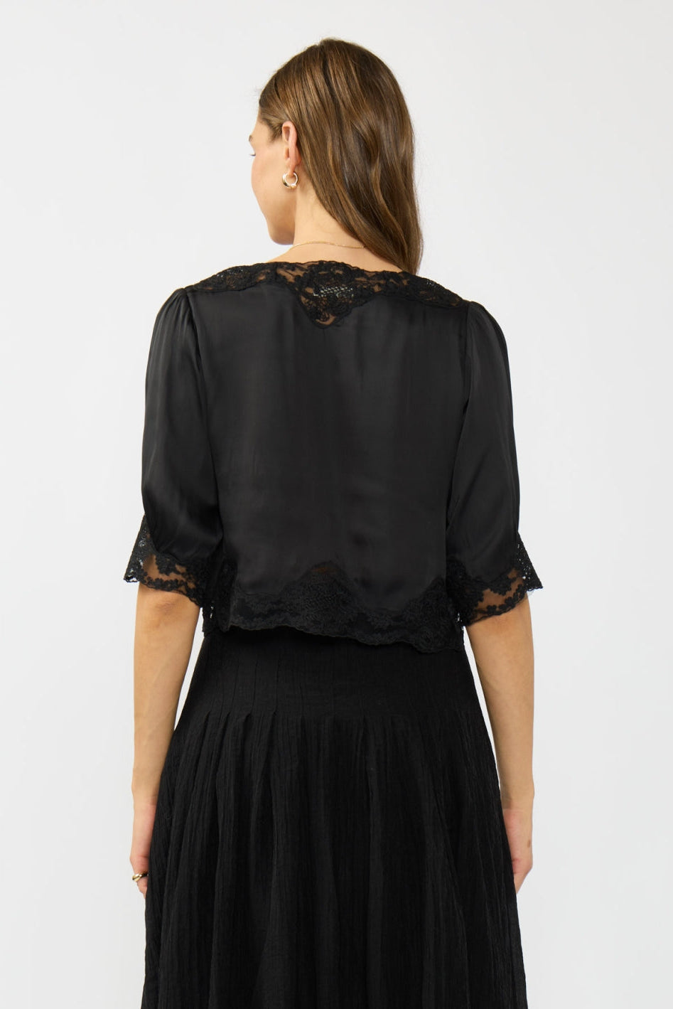 Woman wearing a black blouse with lace details shown from the back on a white background