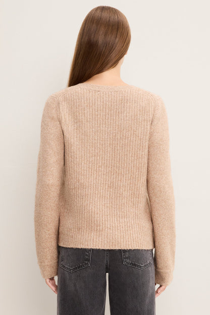 A woman viewed from the back wearing an oatmeal ribbed knit sweater and dark gray jeans, set against a plain off-white background.