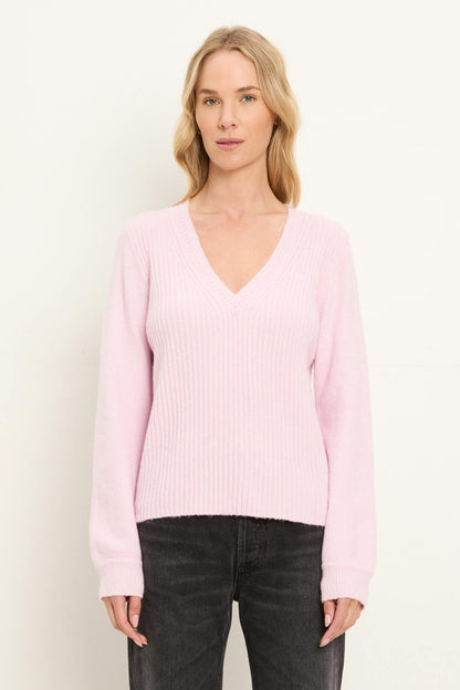 A woman shown from the front wearing a pink tulip colored v neck sweater and washed black jeans on  a white background.