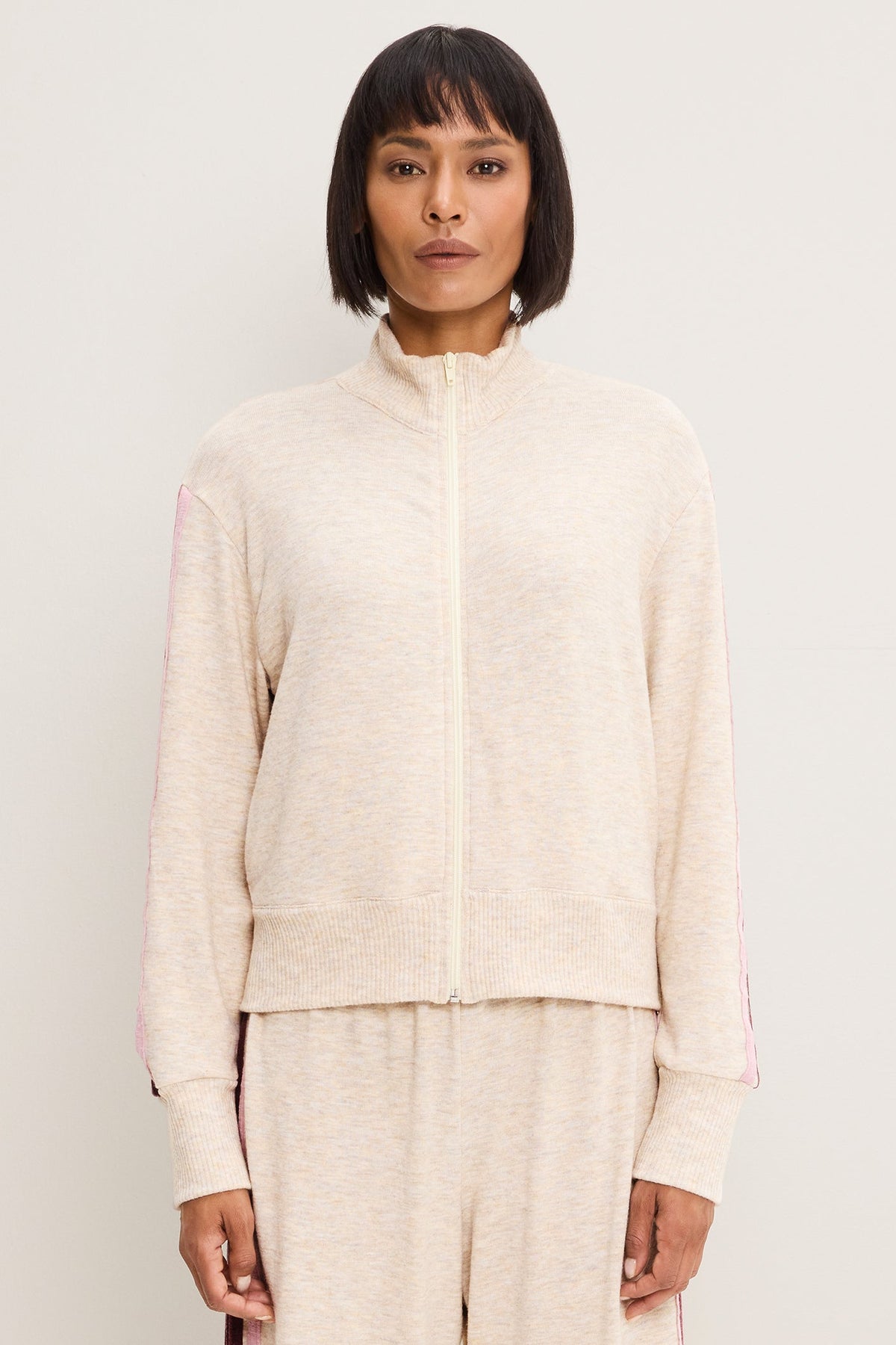 A model wearing a heather oatmeal-colored knit zip-up jacket and matching knit pants against a plain light background.