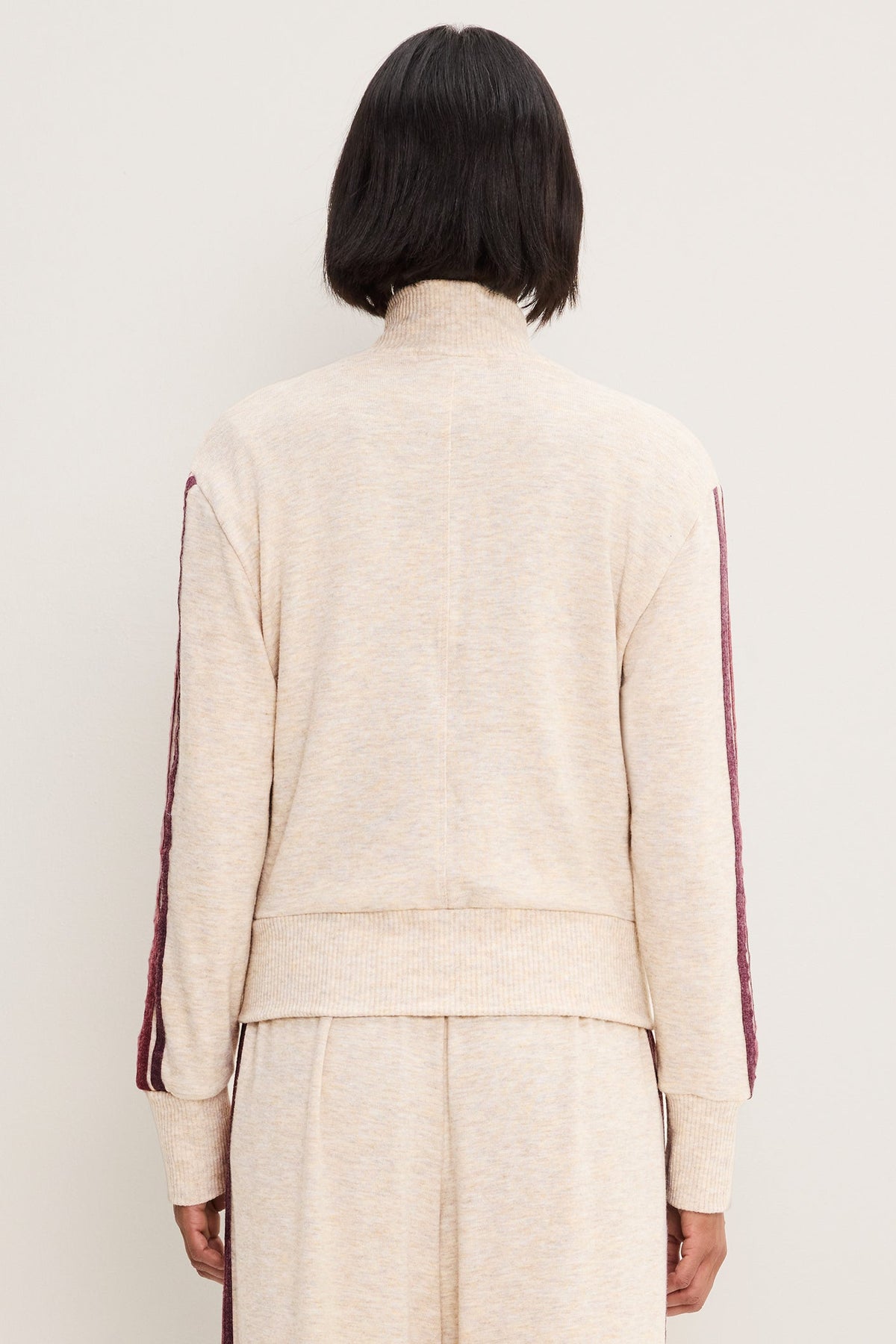 A person shown from the back wearing a heather oatmeal-colored knit mock-neck sweater with burgundy stripes down the sleeves, paired with matching knit pants, against a plain off-white background.