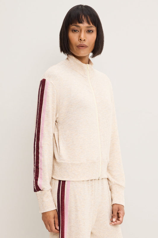 A model wearing a heather oatmeal-colored knit zip-up jacket with a pink and burgundy striped sleeve, paired with matching knit pants, against a plain light gray background.