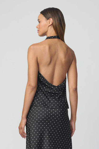 A woman shown from the back wearing a black halter top with a white polka dot pattern and matching skirt against a light gray studio background.