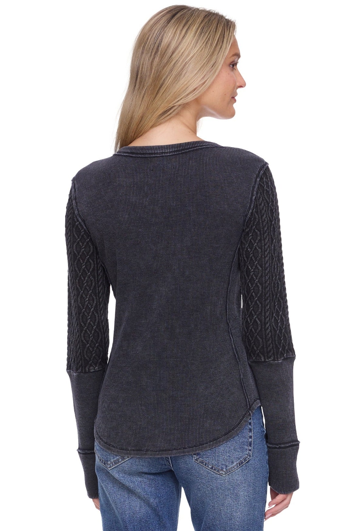 A woman shown from the back wearing a dark charcoal gray long-sleeve top with textured cable-knit sleeves, paired with blue jeans, against a plain white background.