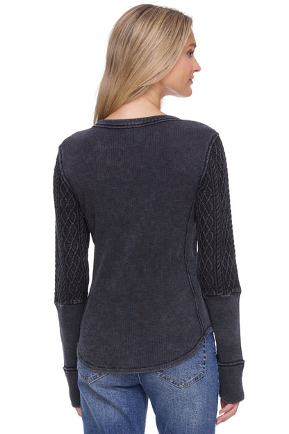 A woman shown from the back wearing a dark charcoal gray long-sleeve top with textured cable-knit sleeves, paired with blue jeans, against a plain white background.