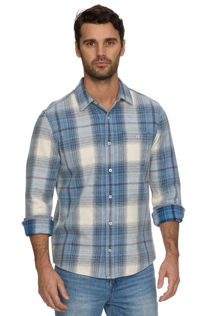 A man wearing a blue and off-white Asheville Vintage Wash plaid button-down shirt with rolled-up sleeves, paired with blue jeans, against a plain white background.