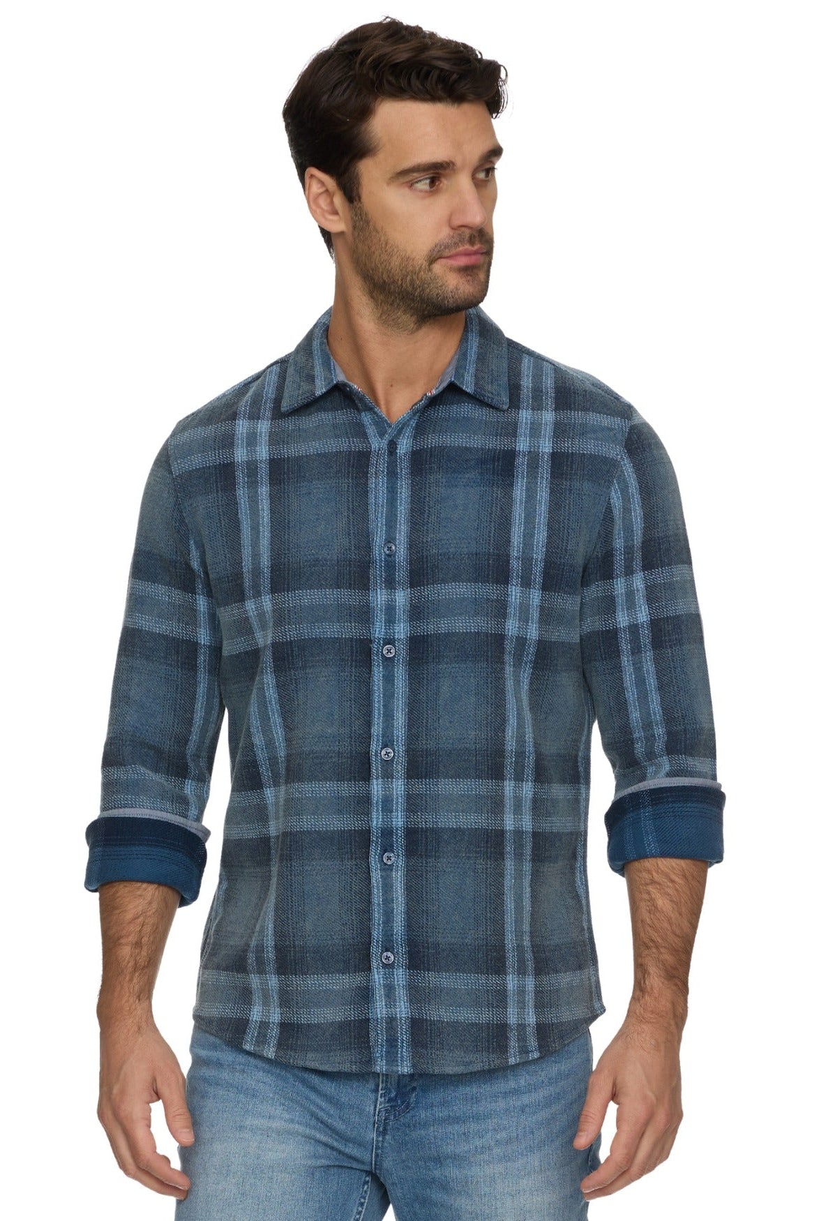A man wearing a Brundidge blue and gray plaid button-down shirt with rolled-up sleeves, paired with blue jeans, against a plain white background.