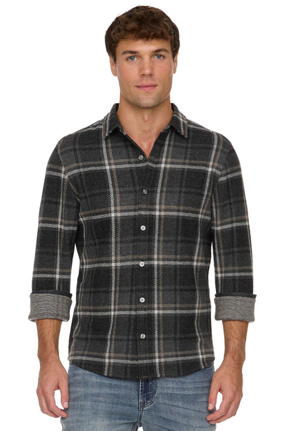 A man wearing a Wadley dark charcoal gray and black plaid button-down shirt with rolled-up sleeves, paired with blue jeans, against a plain white background.