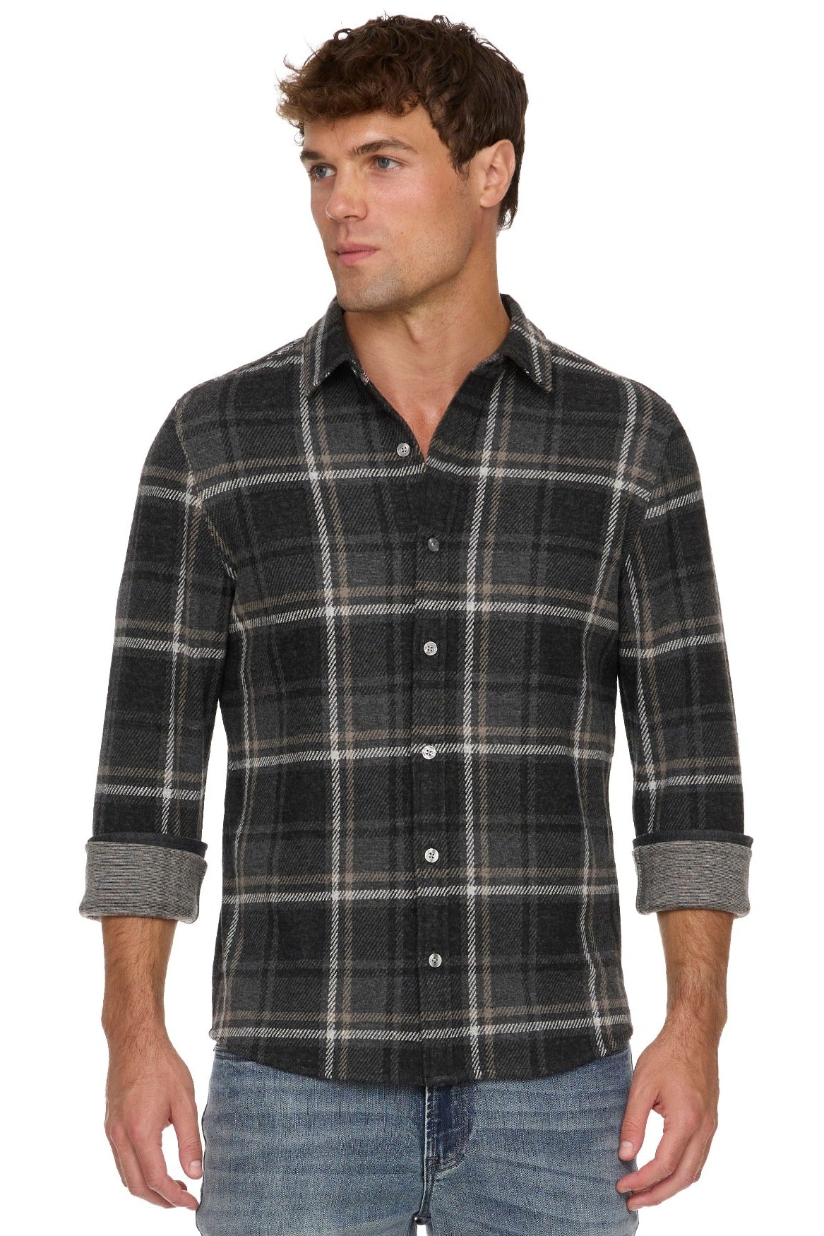 A man wearing a charcoal gray and black plaid button-down shirt with rolled-up sleeves, paired with blue jeans, against a plain white background.