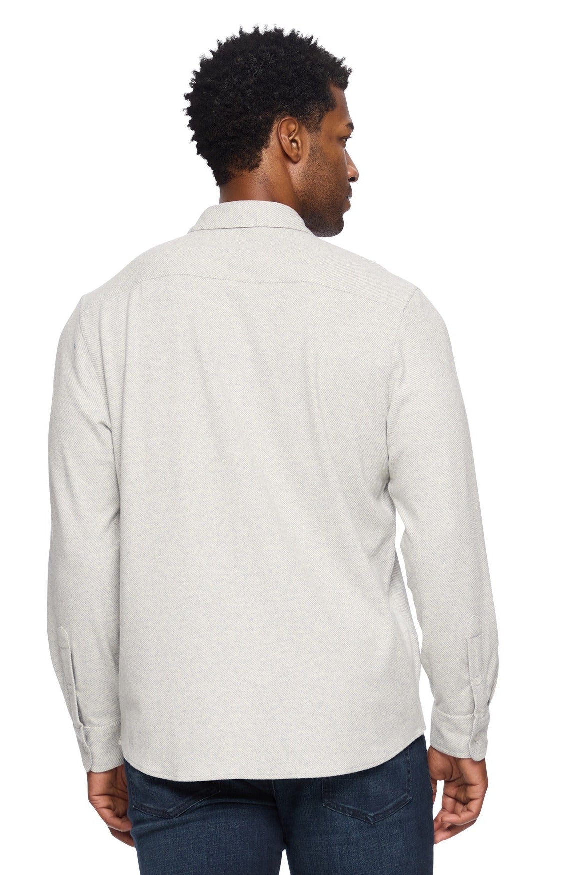 A man viewed from the back wearing a light heather gray twill long-sleeve button-up flannel shirt and dark blue jeans, set against a plain white background.