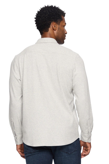 A man viewed from the back wearing a light heather gray twill long-sleeve button-up flannel shirt and dark blue jeans, set against a plain white background.
