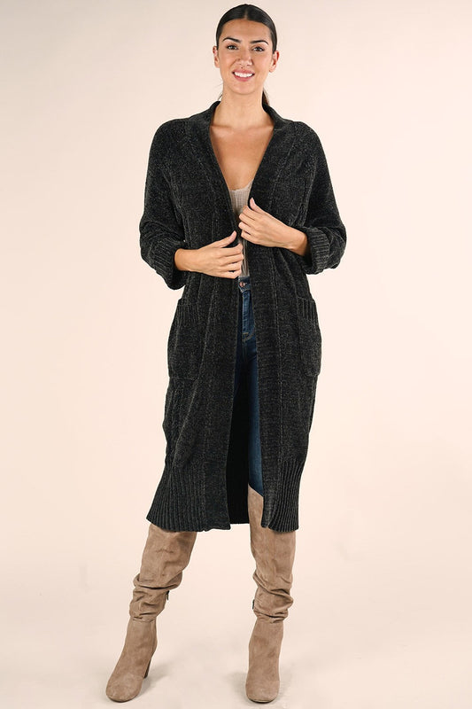 A woman modeling a forest colored open-front knit duster cardigan over a beige top and blue jeans, paired with taupe knee-high boots, against a solid light beige studio background.
