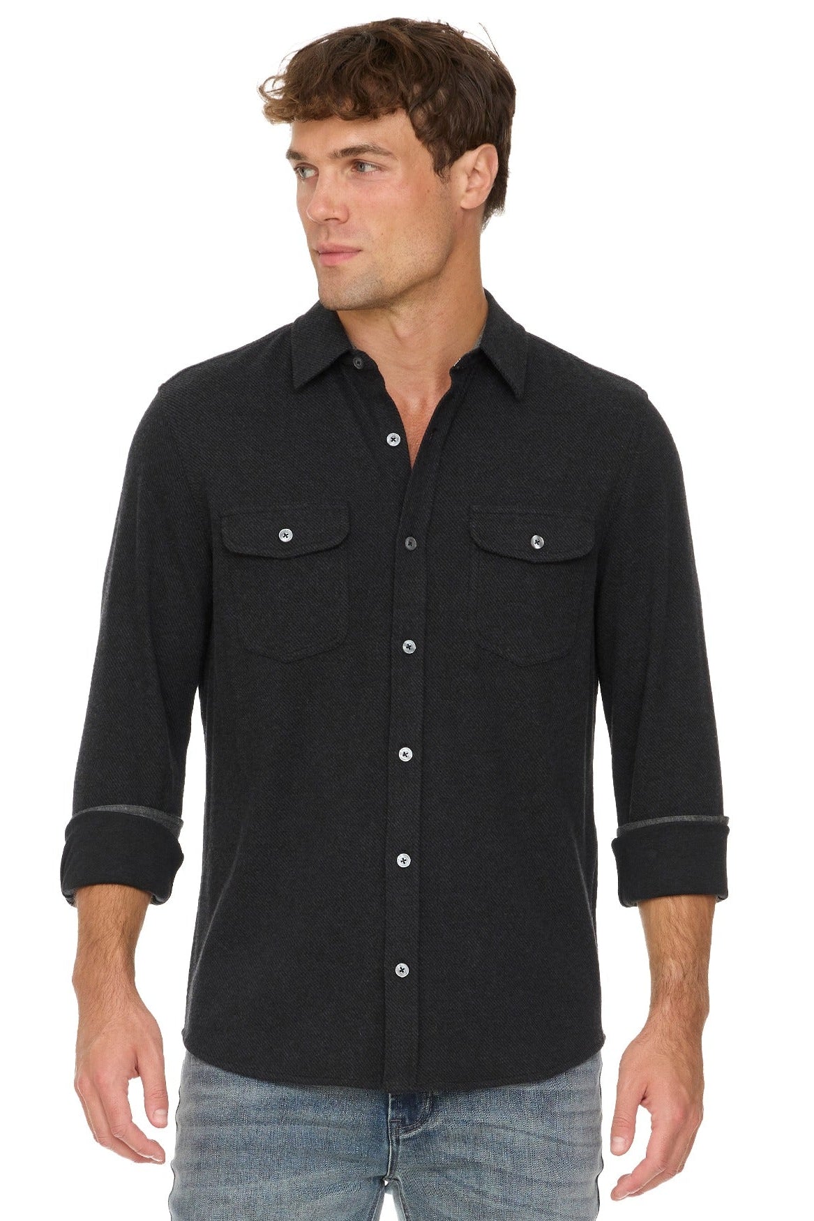 A man wearing a black long-sleeve western-style Hero Twill button-down shirt with two chest pockets and rolled cuffs, paired with blue jeans, against a plain white background.