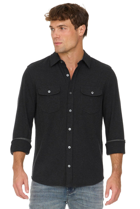 A man wearing a black long-sleeve western-style Hero Twill button-down shirt with two chest pockets and rolled cuffs, paired with blue jeans, against a plain white background.