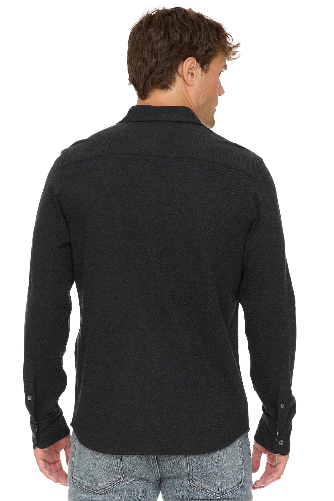 A man viewed from the back wearing a dark charcoal gray long-sleeve knit shirt and light blue jeans against a plain white background.