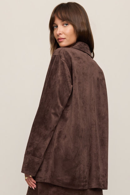 Woman shown from the back wearing a dark chocolate brown suede jacket on a beige background