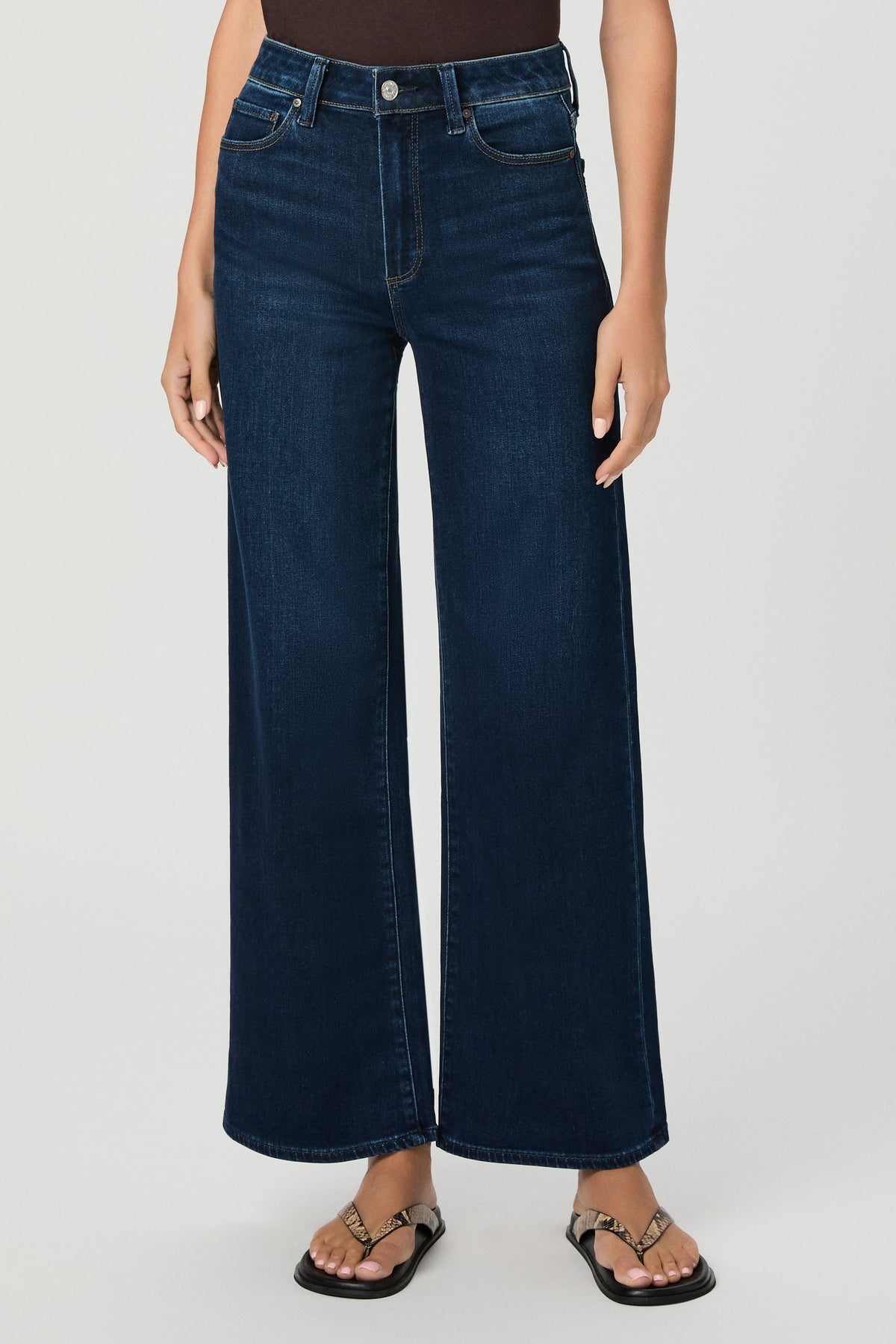 A model wearing amagansett blue wide-leg cropped jeans with a brown top and black sandals, shown from the waist down against a light gray studio background.