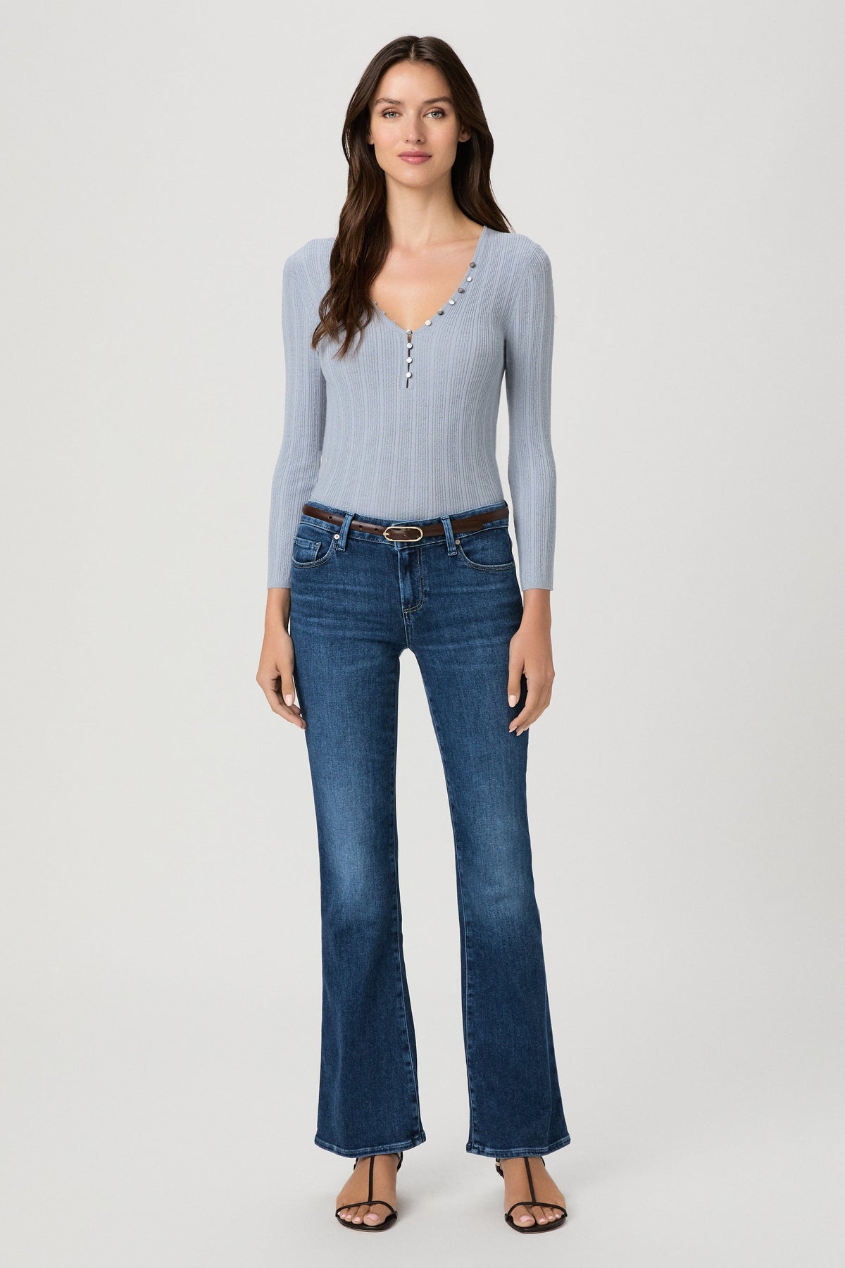 A woman modeling a light blue ribbed long-sleeve henley top and dark blue beachline flare jeans against a plain light gray studio background.