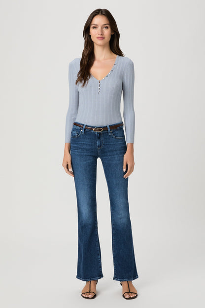 A woman modeling a light blue ribbed long-sleeve henley top and dark blue beachline flare jeans against a plain light gray studio background.