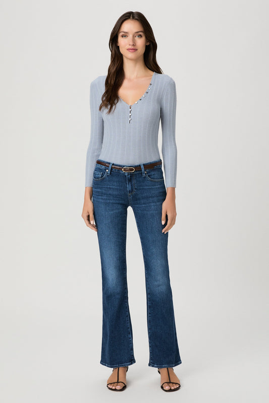 A woman modeling a light blue ribbed long-sleeve henley top and dark blue beachline flare jeans against a plain light gray studio background.