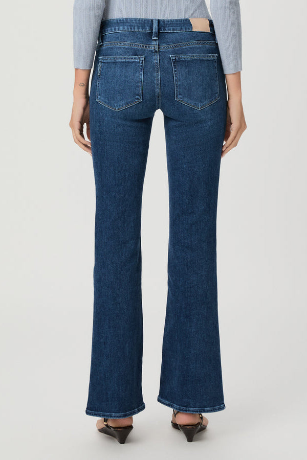 Rear view of a model wearing dark blue beachline high-waisted flare jeans with a light blue striped long-sleeve top and brown pointed-toe heels, against a light gray studio background.