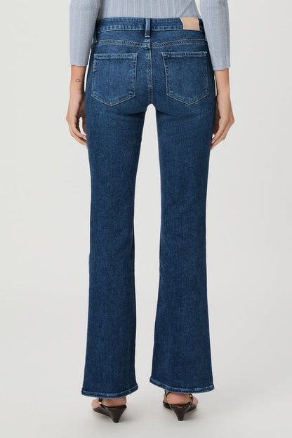Rear view of a model wearing dark blue beachline high-waisted flare jeans with a light blue striped long-sleeve top and brown pointed-toe heels, against a light gray studio background.
