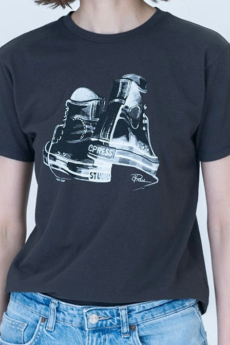 A person wearing a worn black graphic t-shirt with a white and black high-top sneaker illustration on the front, paired with light blue denim jeans.