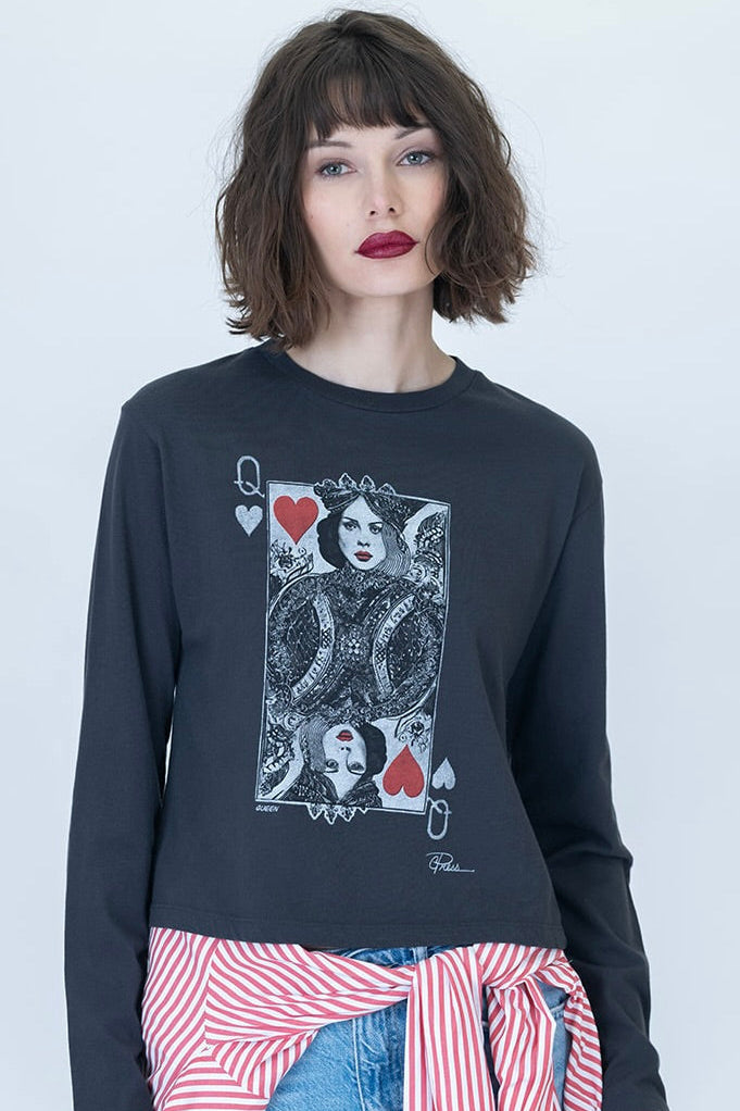 A woman modeling a worn black long-sleeve crewneck tee featuring a graphic print of the Queen of Hearts playing card on the front. She is also wearing a red and white striped shirt tied around her waist and blue jeans, set against a plain light gray studio background.