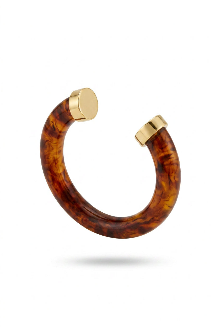 A curved open cuff bracelet featuring a glossy amber-brown tortoiseshell pattern with polished gold-toned metal ends, shown against a plain white background.