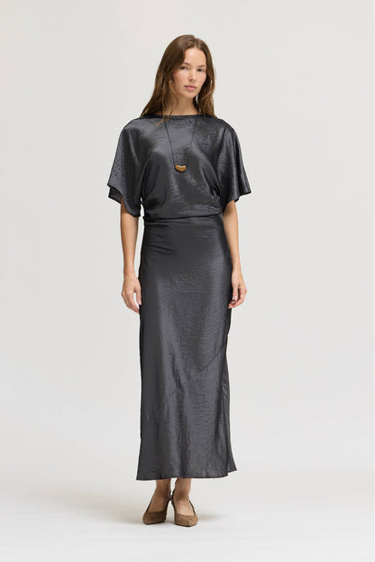 A woman modeling a dark granite wash gray, textured dress consisting of a short-sleeve top and a maxi silhouette paired with brown shoes against a light gray studio background.