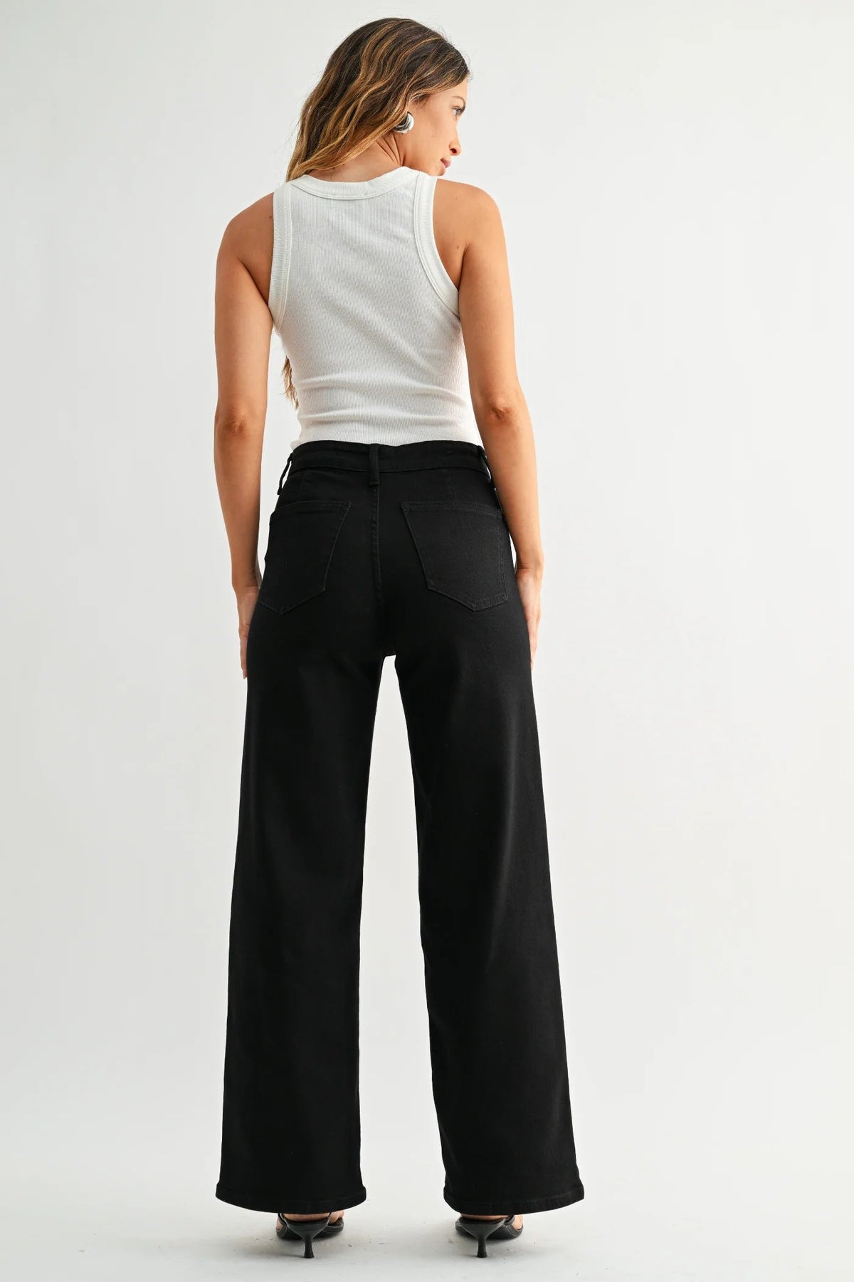 Woman wearing a white sleeveless top and black wide-leg hidden pocket trouser pants on a light gray background