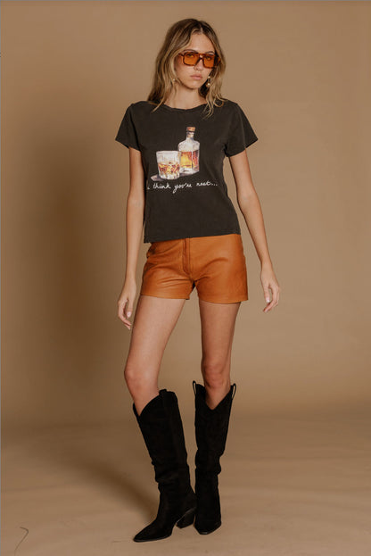 Woman wearing a vintage black "I think you're neat" tshirt featuring an old fashioned drink graphic paired with burnt orange shorts and black boots.