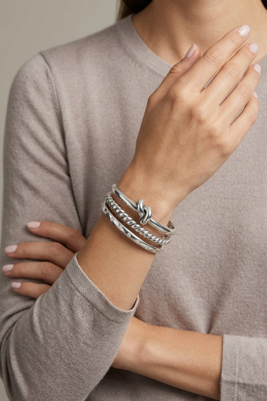 Person wearing silver bracelets on a neutral background
