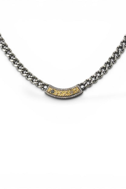 A silver-toned Soleil ID Cuban link chain necklace with a central curved bar set with small clear stones and a textured gold center, shown on a plain white background.