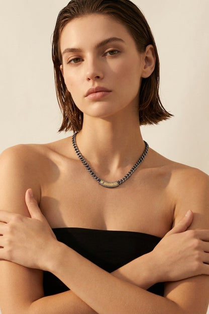 Woman wearing a black strapless top and Soleil ID necklace against a beige background