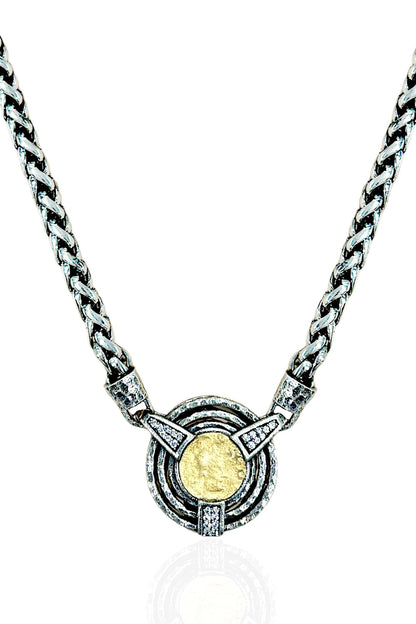 A silver-toned chain necklace with a circular pendant featuring a textured gold coin in the center, surrounded by concentric rings and small clear stones, shown on a white background.