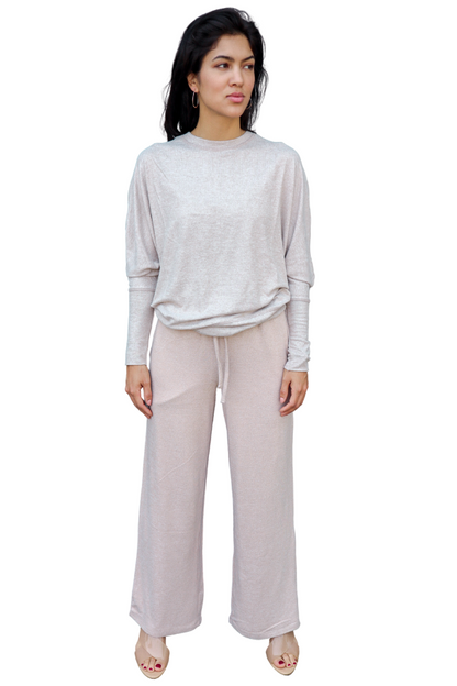 Woman wearing a light pink long-sleeve top and beige wide-leg pants on a white background